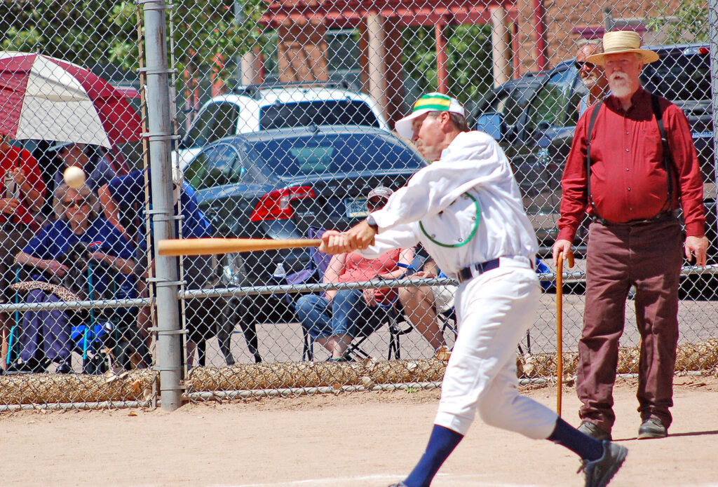 Photo by Larry Ferguson. Neil Chapman of the Heritage Center Springers connects for a hit during the Colorado Vintage Base Ball Association contest on Aug. 6. Umpire Ferril “Mad Dog” Mason stands in the background.