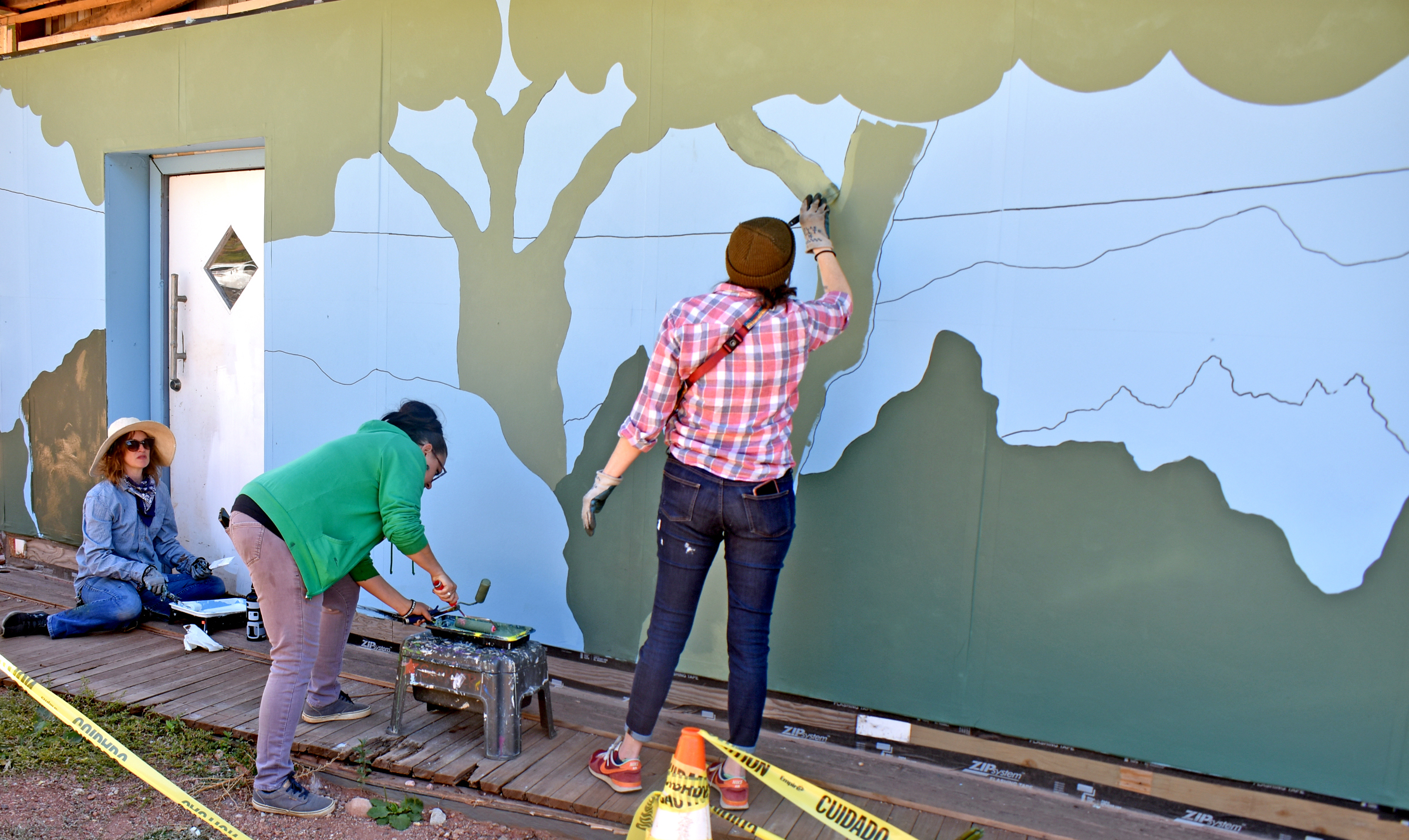 Photo by Rhonda Van Pelt. Organizers and volunteers work on the Hiawatha Gardens mural on Tuesday, Oct. 18. It’s 106 feet long, and is inspired by a vintage postcard featuring the building’s history as a dance hall. From left: Becca Sickbert of the Creative Alliance Manitou Springs; K8e Orr, a project organizer and designer; and volunteer Nicole Riggio.